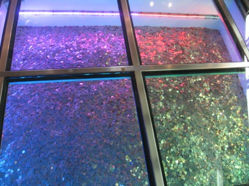 A close-up view of a glass display filled with colorful coins, illuminated by vibrant lights.