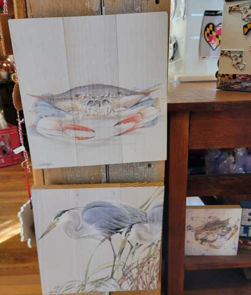 Two wooden panels featuring a crab and a heron, displayed in a shop with various items in the background.