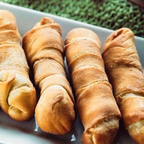 Four golden-brown, twisted bread rolls arranged on a white plate.