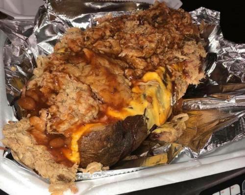 A loaded baked potato topped with shredded chicken, cheese, and baked beans, served in aluminum foil.