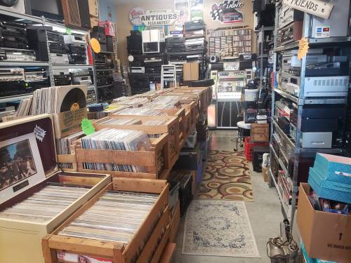 A cozy vintage shop filled with shelves of audio equipment and wooden crates of vinyl records.