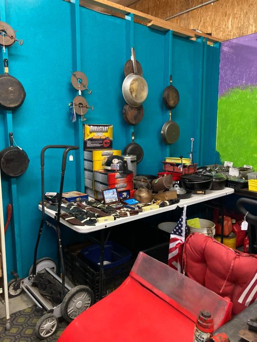 A table filled with various kitchen items and tools, with pots hanging on a blue wall in the background.