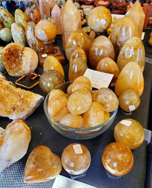 A variety of golden gemstones and crystals displayed on a table, including spheres, polished stones, and points.