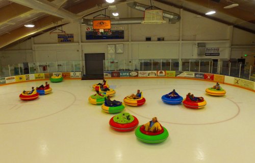 Aerial view of colorful bumper cars on ice, with people enjoying a fun activity in a rink.