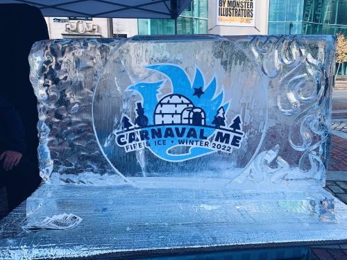 An ice sculpture featuring the logo for "Carnaval Me: Fire & Ice - Winter 2022" with decorative swirls.