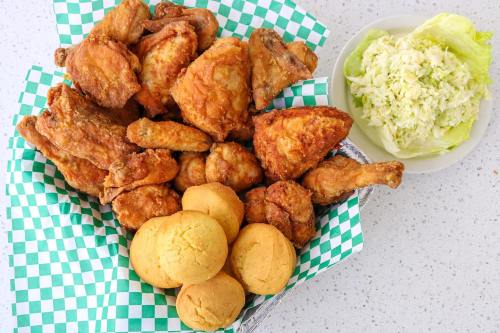 A basket of crispy fried chicken pieces with cornbread muffins and a side of coleslaw on a plate.
