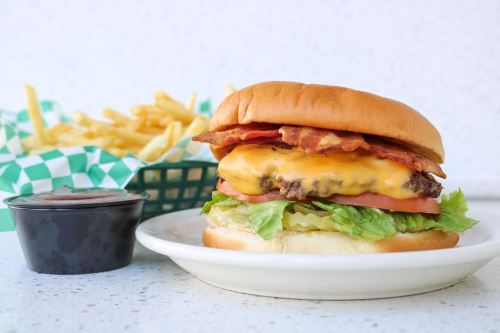 A juicy cheeseburger with bacon, lettuce, and tomato, served with a side of fries and dipping sauce.
