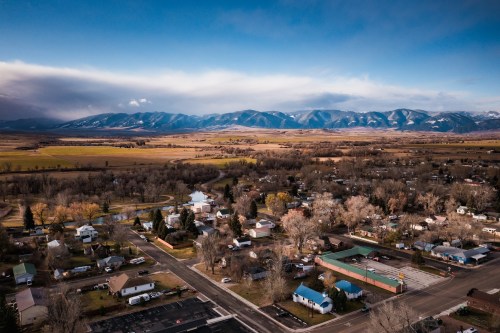 Aerial view of a small town surrounded by mountains and fields, with a river winding through the landscape.