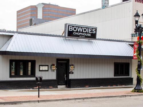 Exterior of Bowdies Chophouse, featuring a gray and black facade with a sign, wreaths, and nearby parking meters.