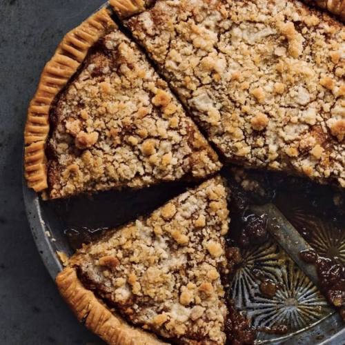 A freshly baked pie with a crumbly topping, sliced into pieces, resting in a metal pie dish.