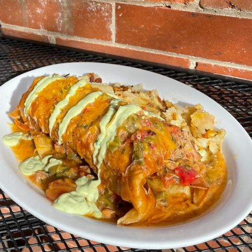 A plate of enchiladas topped with sauce and drizzled with green crema, served with a side of crispy potatoes.