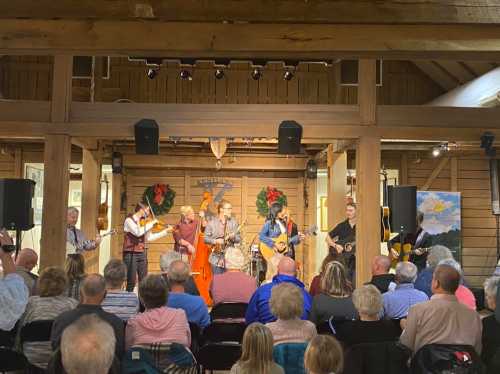 A lively band performs on stage in a rustic venue, with an audience enjoying the music. Holiday decorations are visible.