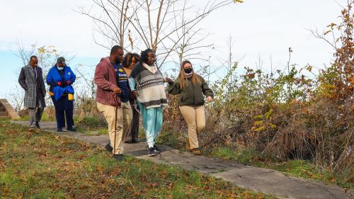 A group of five people walking along a path in a natural setting, surrounded by trees and autumn foliage.