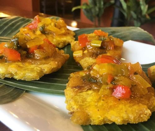 Four tostones topped with colorful vegetable salsa, served on a banana leaf.