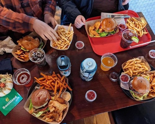 A table with burgers, fries, drinks, and condiments, with hands reaching for food.