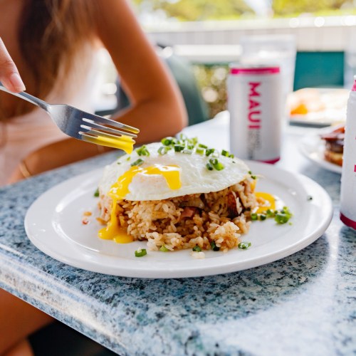 A plate of fried rice topped with an egg and green onions, with a fork poised to take a bite.