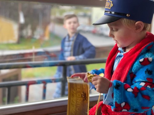 A young child in a blue hat and red robe holds a golden ticket, while another child stands in the background.