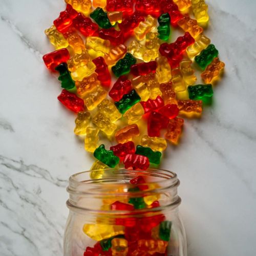 A jar spilling colorful gummy bears in red, yellow, and green onto a marble surface.