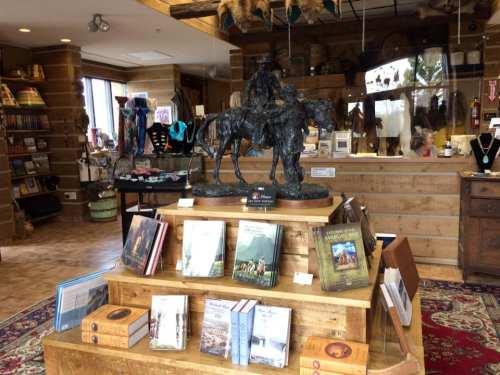 A wooden display with books and a bronze statue of a horse and rider in a cozy gift shop setting.