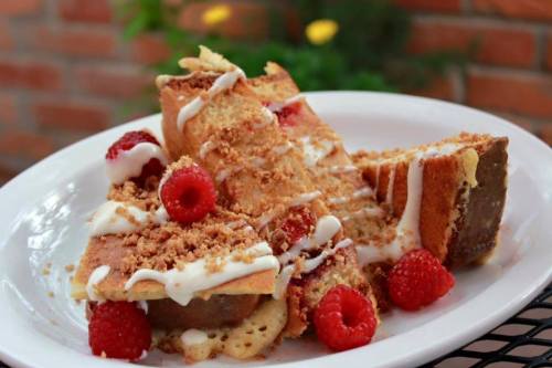 A plate of dessert featuring layered cake, raspberries, and a drizzle of cream, garnished with crunchy topping.