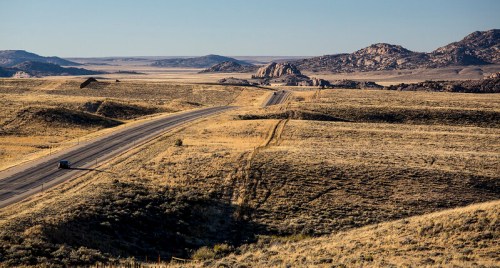 A winding road stretches through a vast, open landscape with rocky formations and distant mountains under a clear sky.