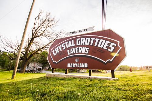 Sign for Crystal Grottoes Caverns of Maryland, featuring bold lettering and a scenic background.