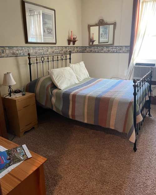 A cozy bedroom featuring a metal bed frame, striped blanket, nightstand, and window with natural light.