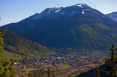 A scenic view of a small town nestled in a valley, surrounded by lush green mountains and snow-capped peaks.