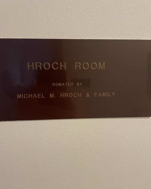 Plaque on a wall reading "HROCH ROOM" with "DONATED BY MICHAEL M. HROCH & FAMILY" engraved below.