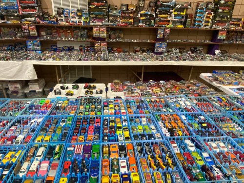 A vibrant display of toy cars in blue bins, with shelves of collectible cars in the background.