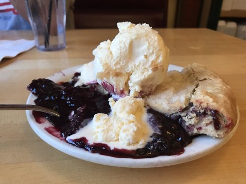 A plate with a slice of berry cobbler topped with vanilla ice cream and a side of berry sauce.