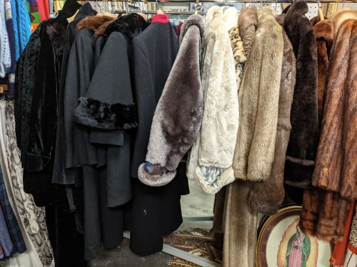 A collection of various fur and wool coats hanging on a rack, showcasing different textures and colors.