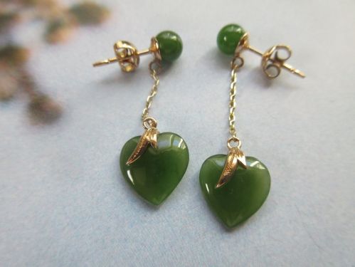 Green heart-shaped earrings with gold accents and dangling chains, featuring round green beads at the top.