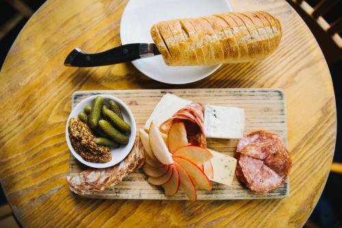 A wooden board with sliced bread, cheese, salami, apple slices, pickles, and mustard on a table.