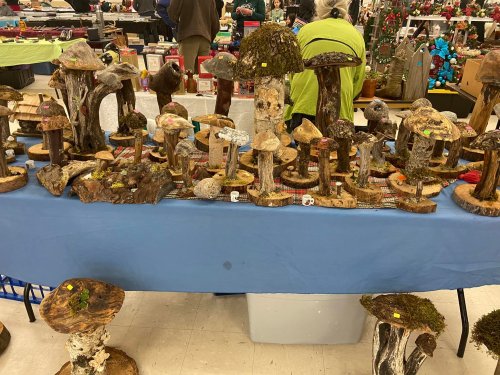 A display of various decorative wooden mushrooms on a blue table at a craft fair.