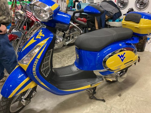 A blue and yellow scooter featuring the West Virginia Mountaineers logo, parked in a garage among other vehicles.
