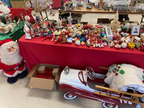 A festive display of holiday decorations, including ornaments, figurines, and a vintage toy fire truck, with a Santa figure nearby.