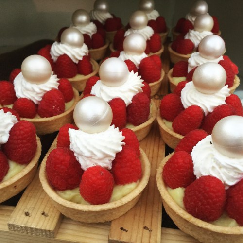 A close-up of tartlets filled with cream and topped with raspberries and shiny white pearls.