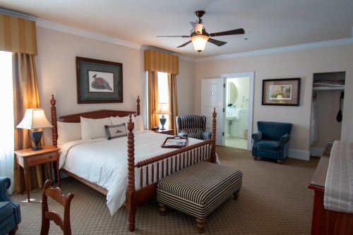 A cozy hotel room featuring a four-poster bed, armchairs, and an en-suite bathroom. Warm lighting and decor create a welcoming atmosphere.