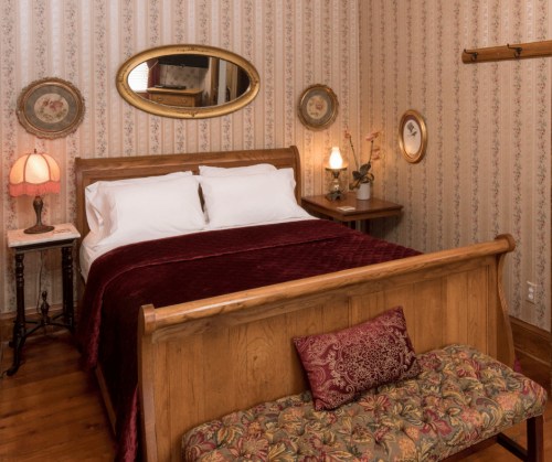 Cozy bedroom with a wooden bed, floral wallpaper, and vintage decor, featuring a bedside lamp and a decorative bench.