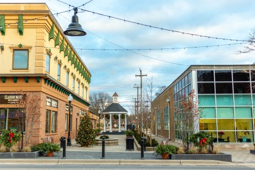 A charming town square with a gazebo, festive decorations, and modern buildings under a cloudy sky.