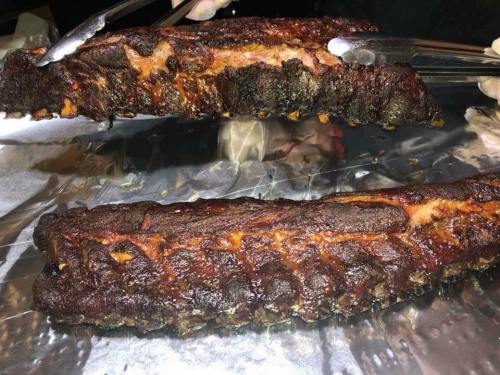 Two pieces of smoked ribs on aluminum foil, showing a dark, charred exterior and juicy meat.