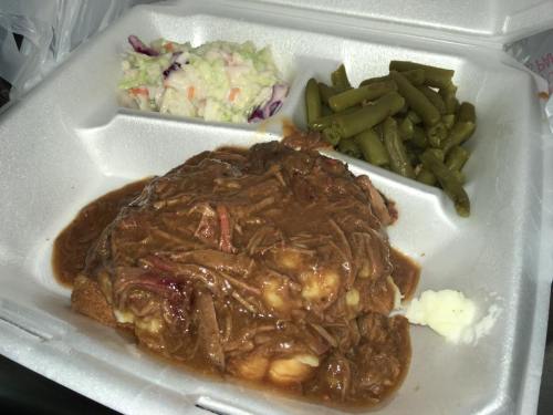 A takeout container with mashed potatoes, beef stew, green beans, and coleslaw.