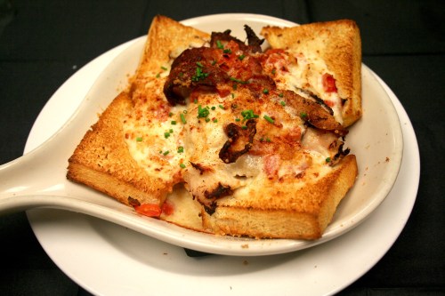 A dish featuring toasted bread filled with creamy sauce, meat, and garnished with herbs, served in a white bowl.