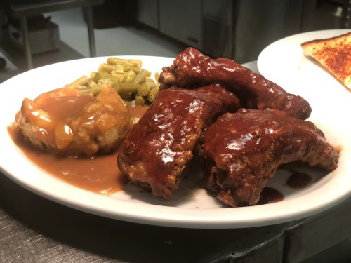 A plate of barbecue ribs with green beans and mashed potatoes topped with gravy.