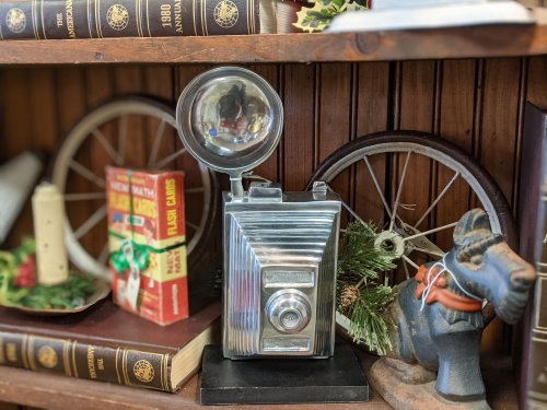 A vintage camera on a shelf surrounded by books, a toy horse, and holiday decorations.