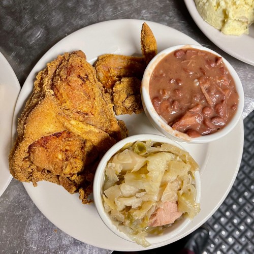 A plate of fried chicken with sides of red beans and cabbage on a metal table.