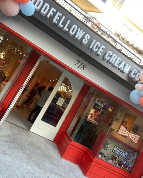 Exterior of Oddfellows Ice Cream Co. with a colorful entrance and balloons, featuring people inside. Address: 718.