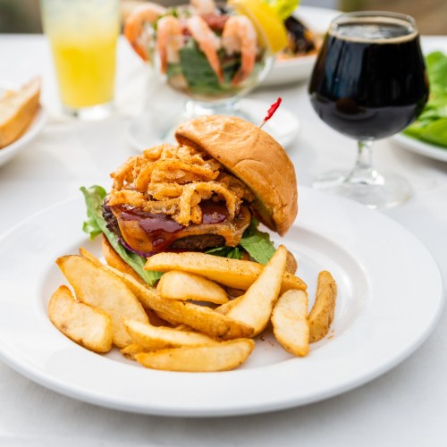 A juicy burger topped with crispy onions on lettuce, served with golden fries and a dark beverage in the background.