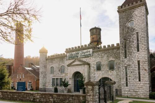 Historic stone building with turrets, featuring a sign for "Old Taylor Distillery," surrounded by trees and a chimney.
